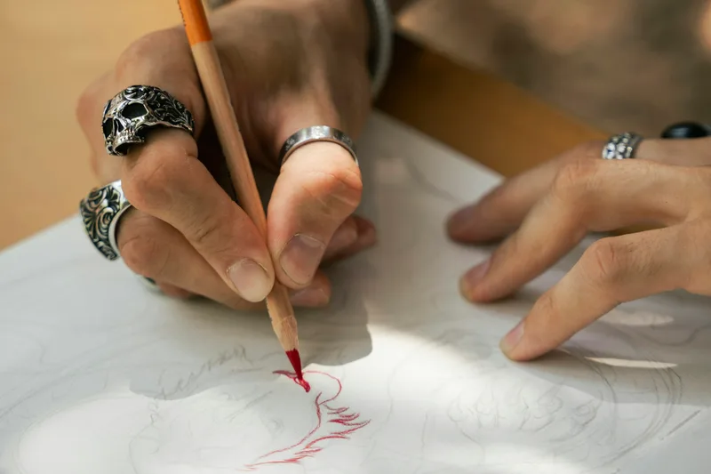 A ringed hand drawing a fine red line across a sheet of white paper